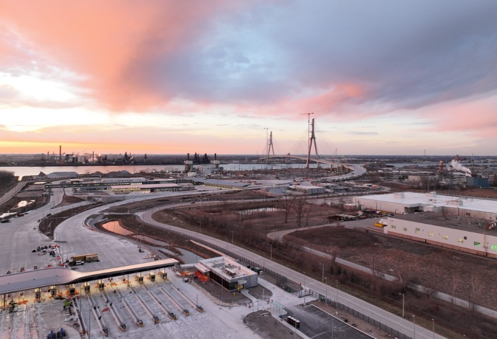 Une photo des voies de péage du pont international Gordie-Howe avec le pont en arrière-plan au coucher du soleil.